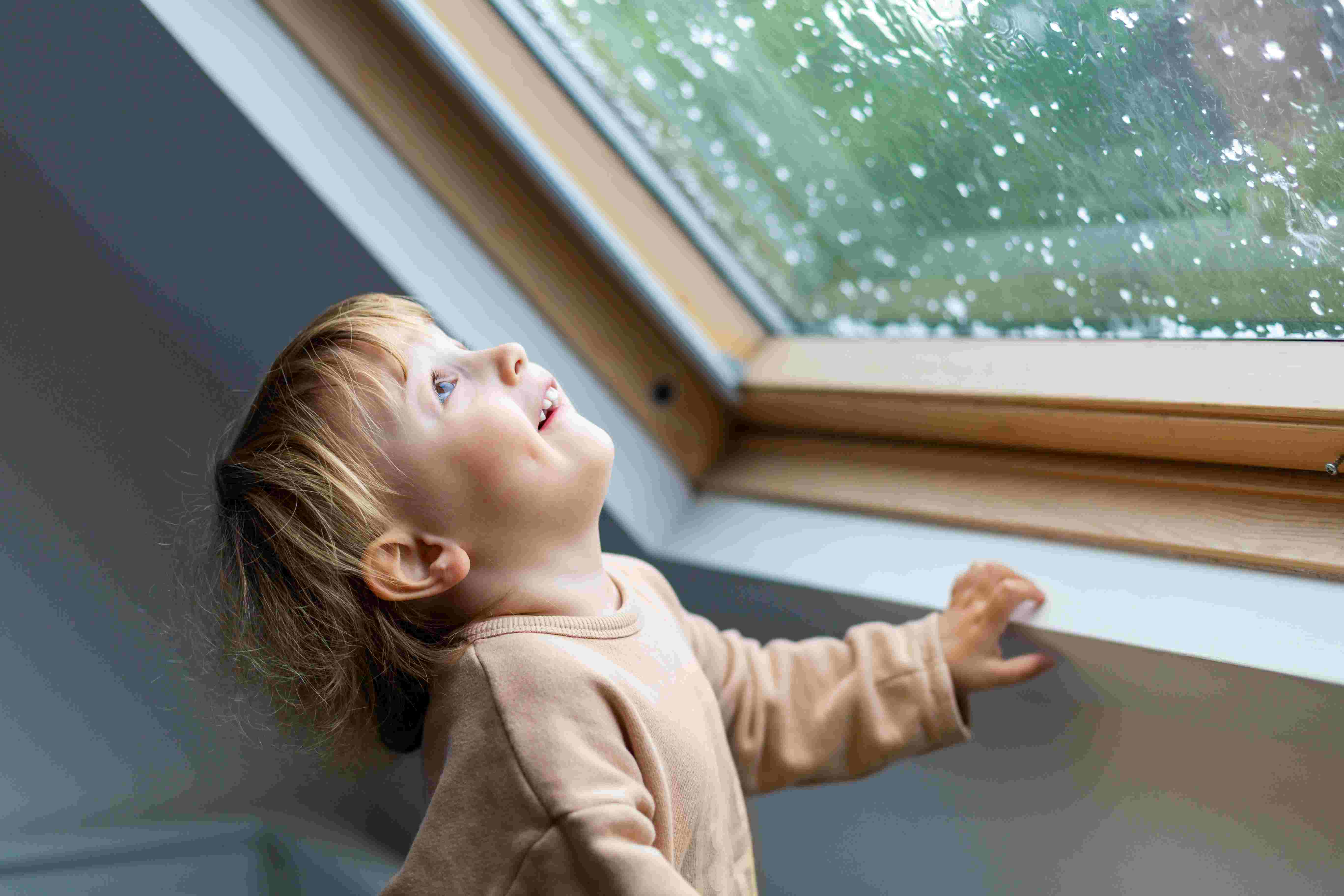 Little preschool boy staying home in bad weather and looking with interest through window on raindrops and hail, idoors.